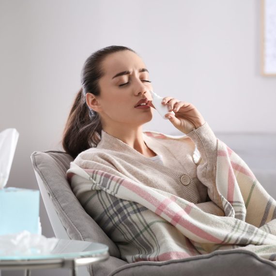 Sick young woman using nasal spray at home