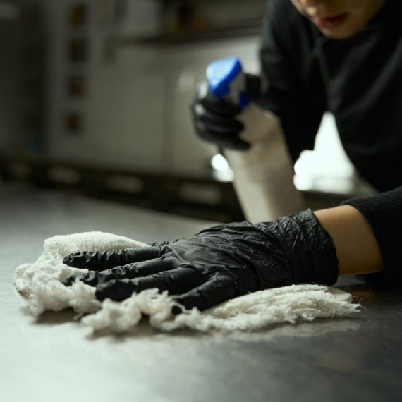 Woman in protective gloves washes a cutting table in a restaurant kitchen, she uses a spray with disinfectant